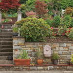 An elaborate hardscape of a retaining wall with a stone staircase and garden landscape all around