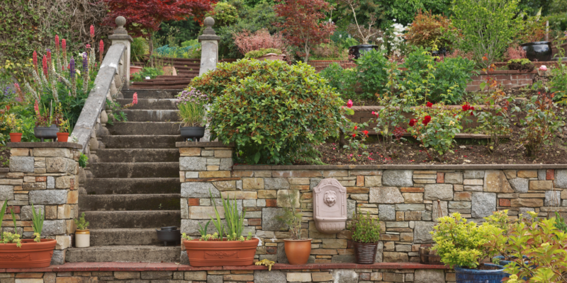 An elaborate hardscape of a retaining wall with a stone staircase and garden landscape all around