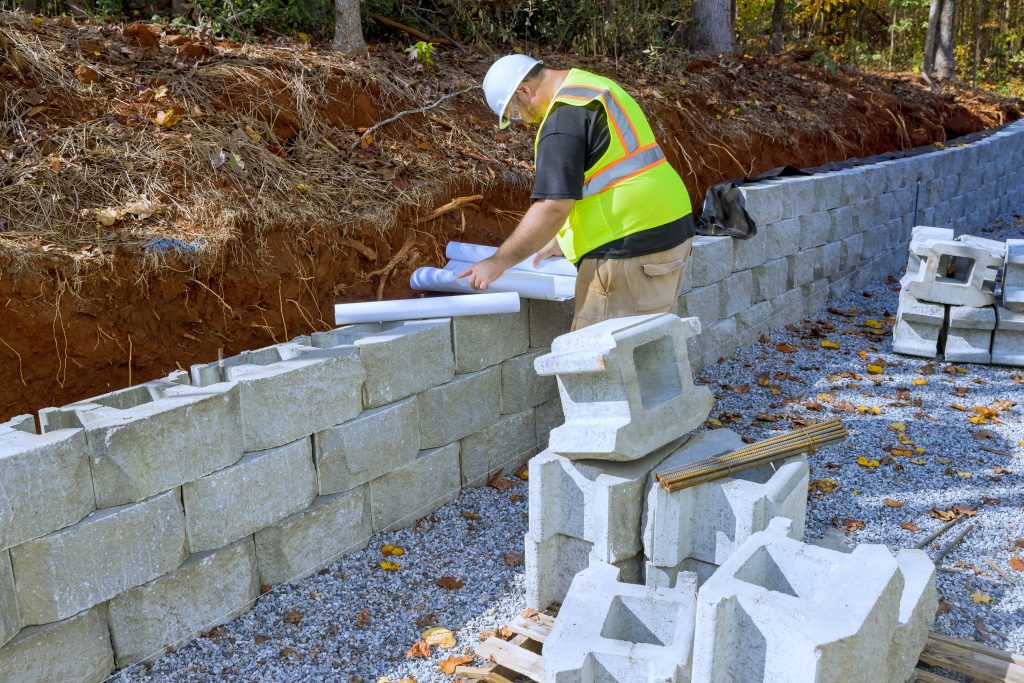 An adult is standing next to a retaining wall under construction and reviewing blueprints for a retaining wall contractor in Roanoke, VA