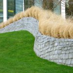 Lush green grass meets a stacked stone wall, topped with tan ornamental grass, acting as erosion control in Roanoke.